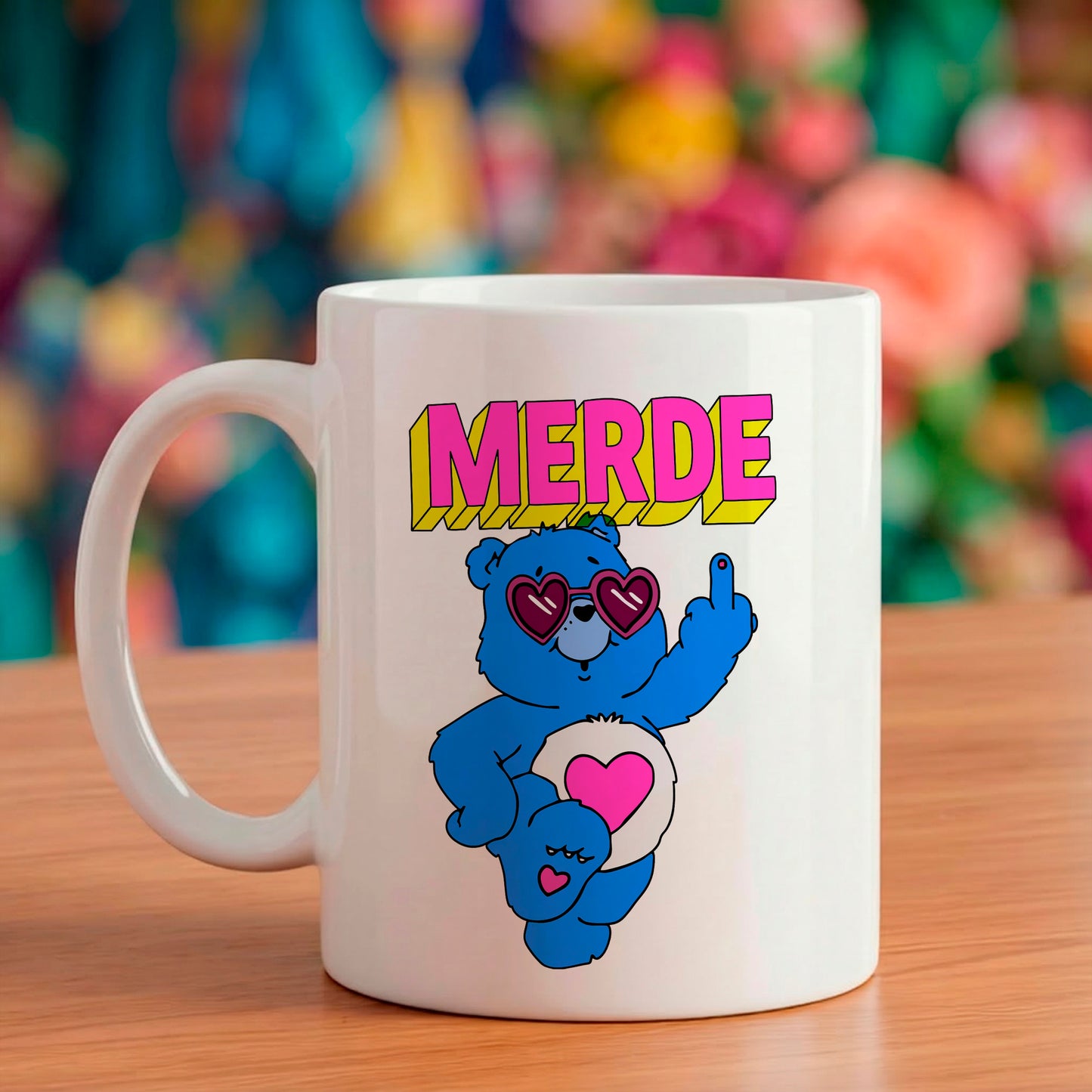 Mug en céramique blanc avec illustration rétro d'un nounours bleu portant des lunettes en forme de cœur faisant un doigt d'honneur avec le texte MERDE écrit au-dessus.