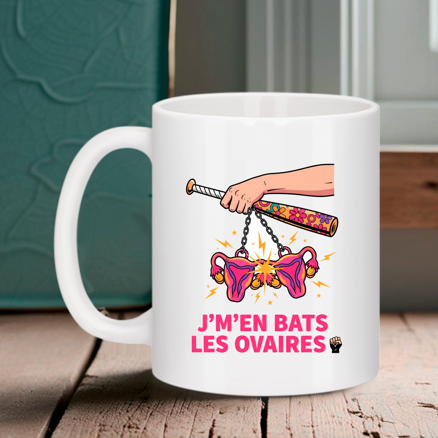 Mug blanc Bruhle avec une illustration d'une main tenant une batte de baseball à fleurs avec des ovaires suspendus par des chaînes, texte rose J'm'en bats les ovaires.