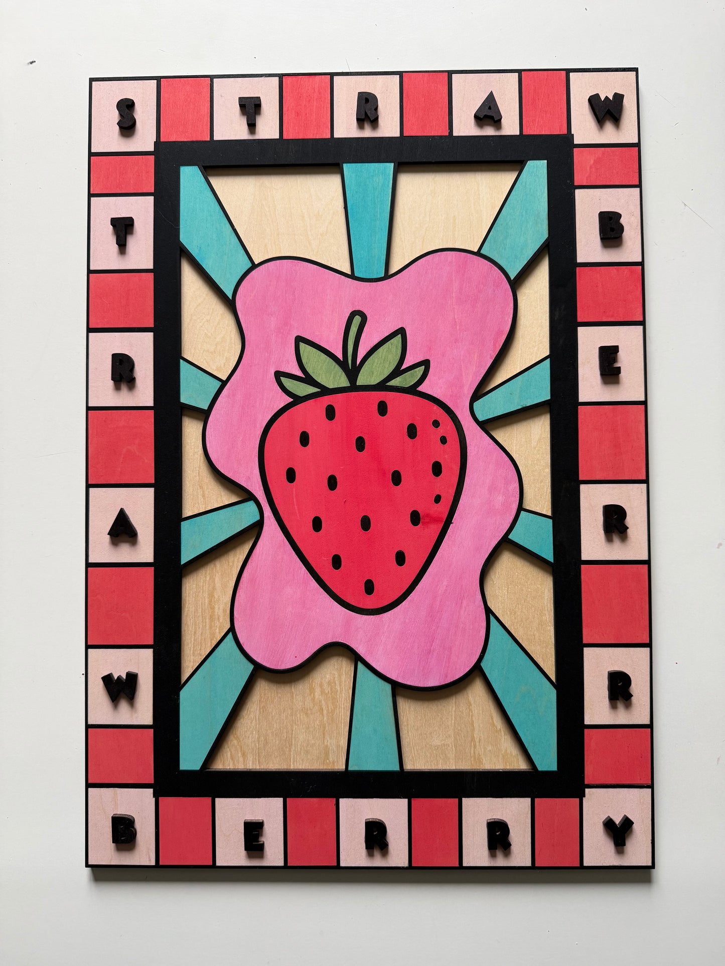Gros plan sur la découpe laser et la peinture artisanale d'un tableau fraise en bois de bouleau, montrant le relief des lettres.