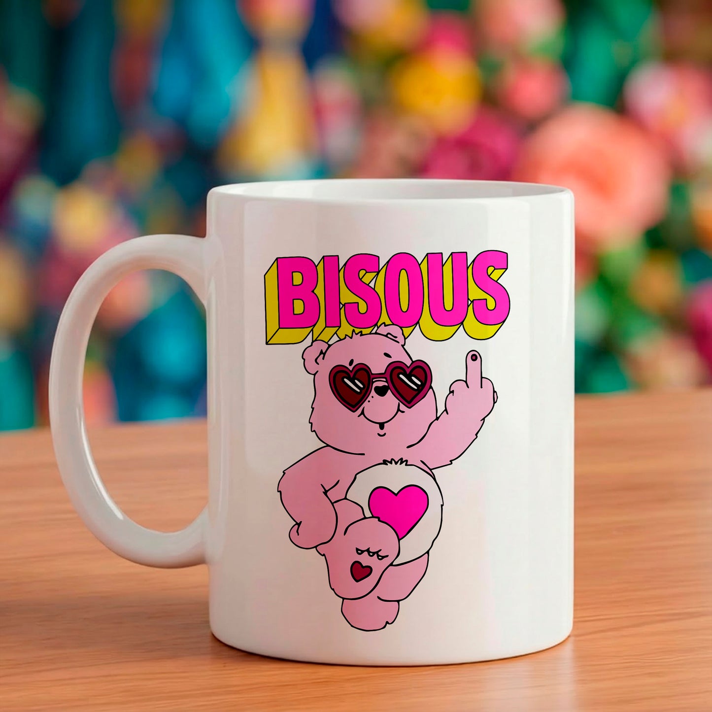 Mug en céramique blanc illustré d'un nounours rose portant des lunettes en forme de cœur faisant un doigt d'honneur avec le mot BISOU écrit en style rétro au-dessus.