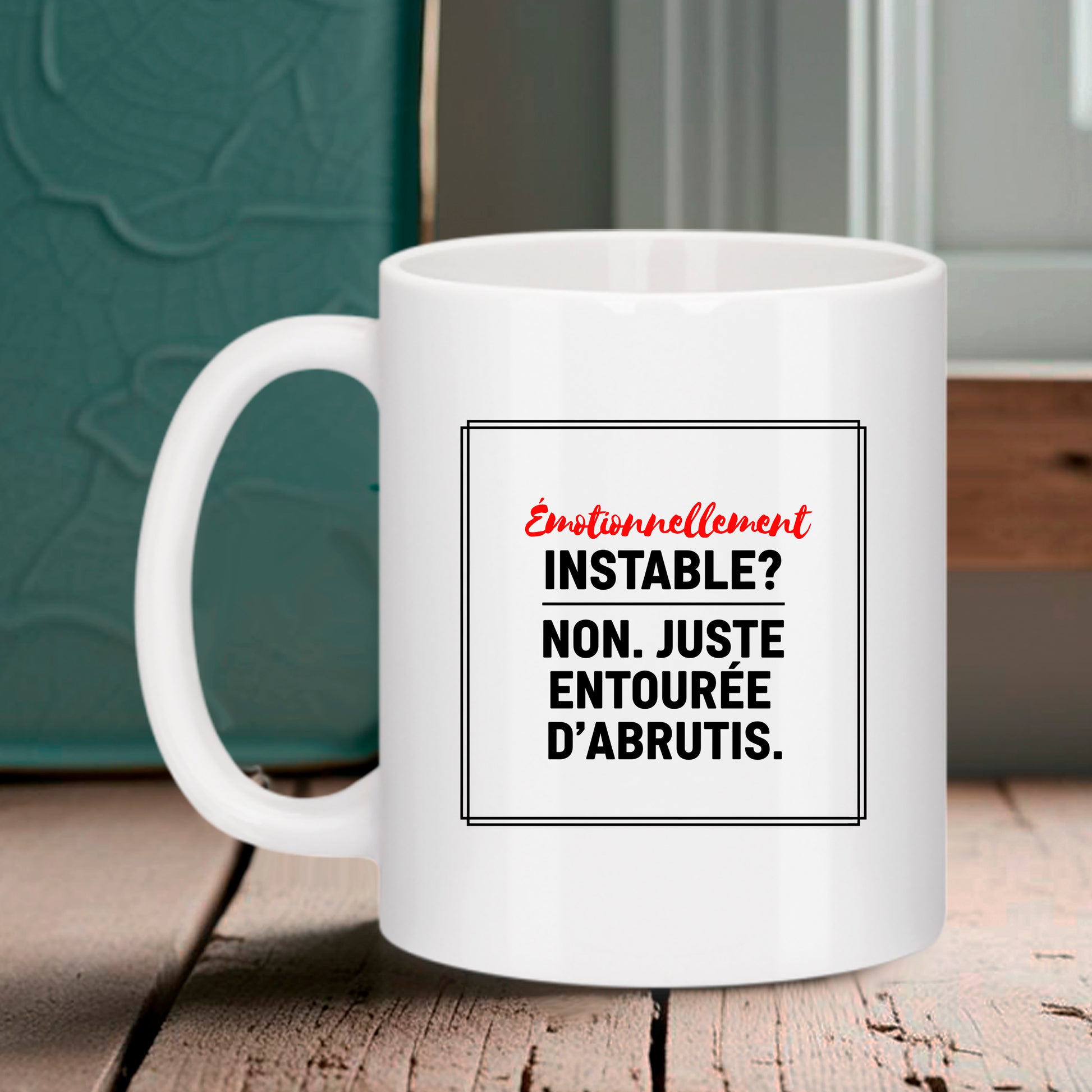Mug blanc Bruhle avec un cadre noir contenant le texte : Émotionnellement INSTABLE ? en rouge, suivi de NON. JUSTE ENTOURÉE D'ABRUTIS. en noir.