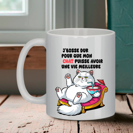 Tasse blanche Bruhle illustrant un gros chat blanc sur un canapé rose avec un cocktail et le texte : J'BOSSE DUR POUR QUE MON CHAT PUISSE AVOIR UNE VIE MEILLEURE.