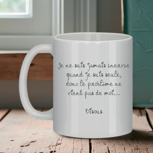 Tasse blanche Bruhle avec un texte noir en cursive : Je ne suis jamais énervée quand je suis seule, donc le problème ne vient pas de moi... Bisous.