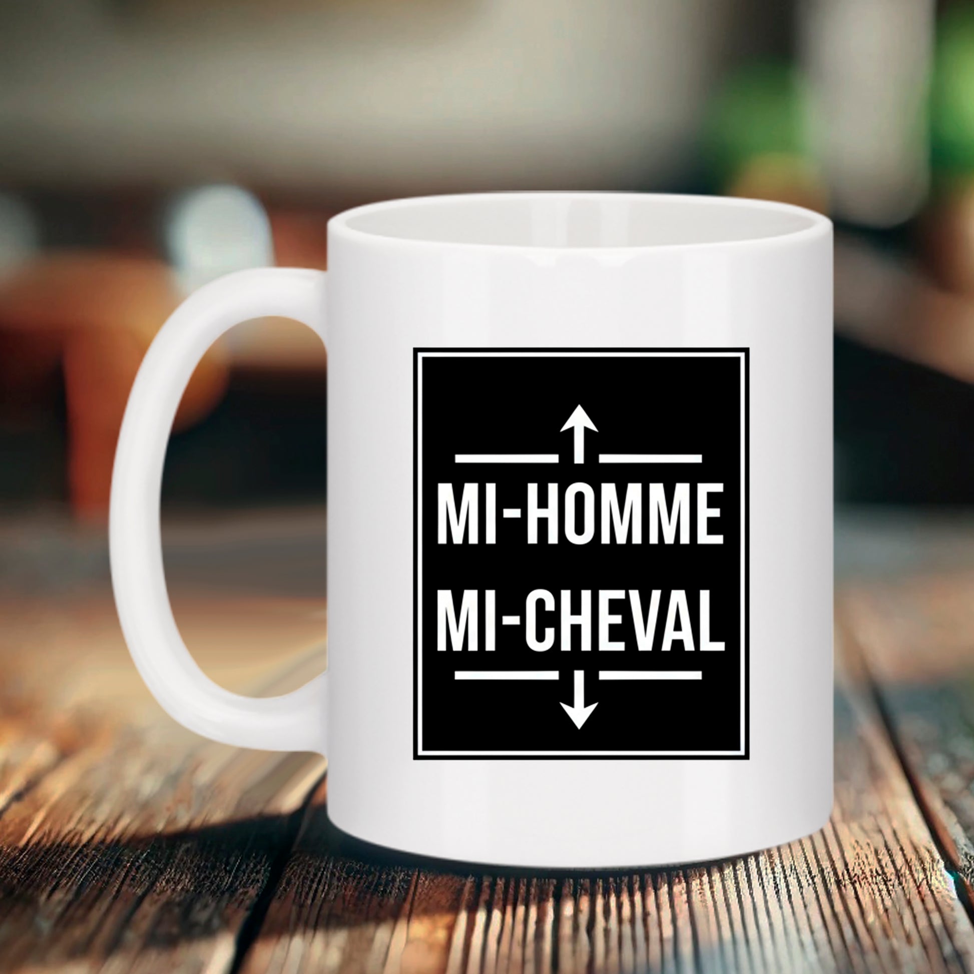 Mug blanc en céramique Bruhle posé sur une table en bois, affichant un design graphique noir carré avec l'inscription humoristique en blanc "MI-FEMME MI-CHIEUSE" encadrée par une flèche vers le haut et une flèche vers le bas.