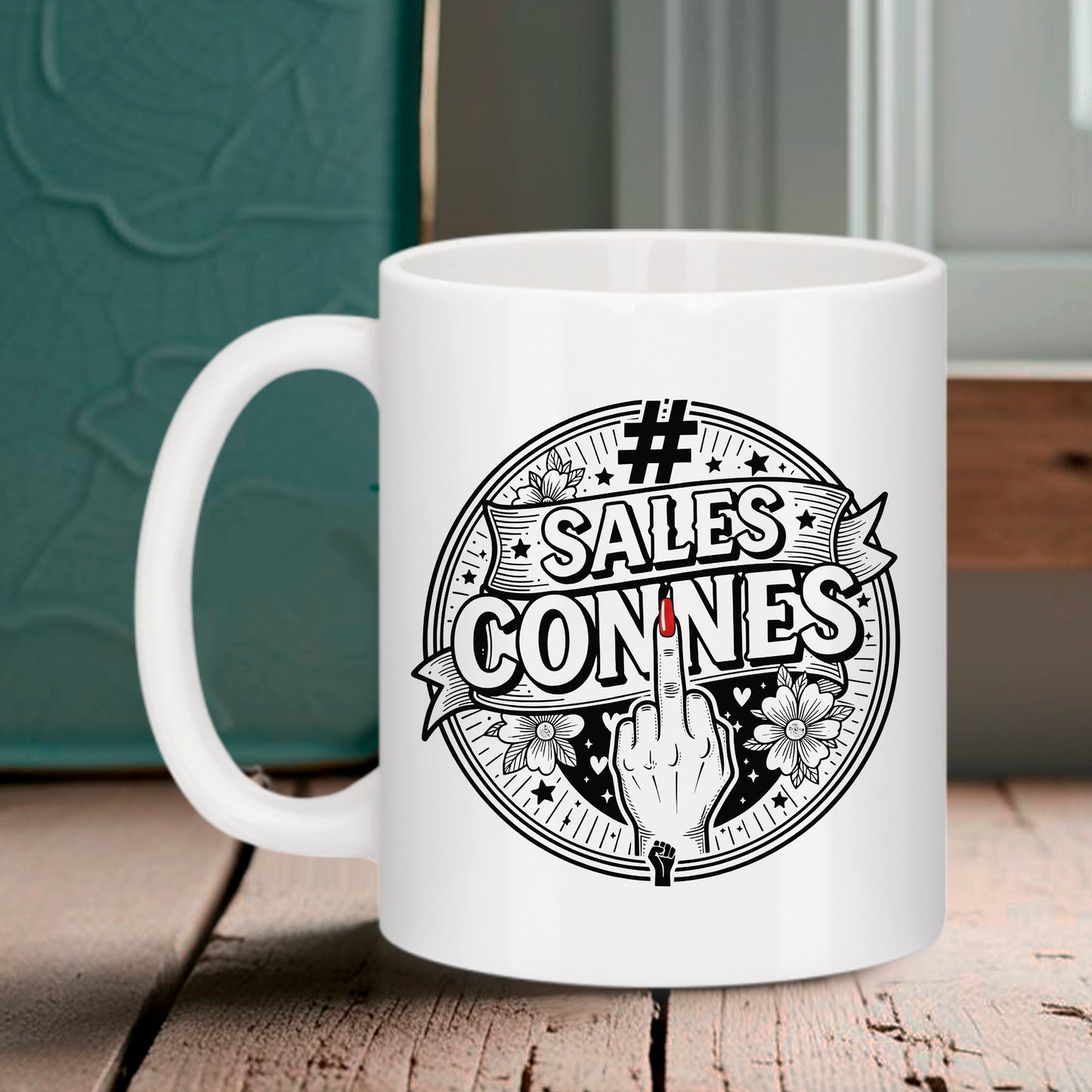 Tasse blanche Bruhle avec un logo circulaire noir style tatouage affichant le texte #SALES CONNES, des fleurs, et un doigt d'honneur avec l'ongle rouge au centre.