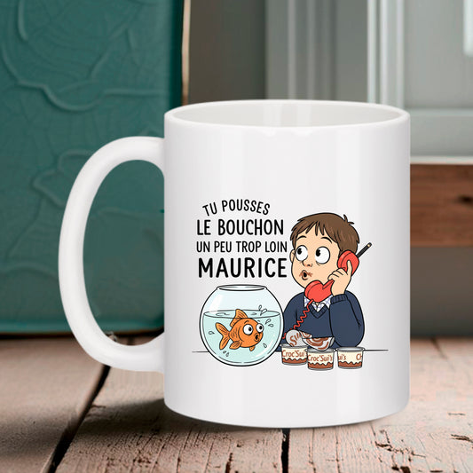 Tasse blanche Bruhle illustrant un petit garçon avec un téléphone rouge devant un bocal de poisson rouge et des pots de crème dessert, avec le texte : TU POUSSES LE BOUCHON UN PEU TROP LOIN MAURICE.