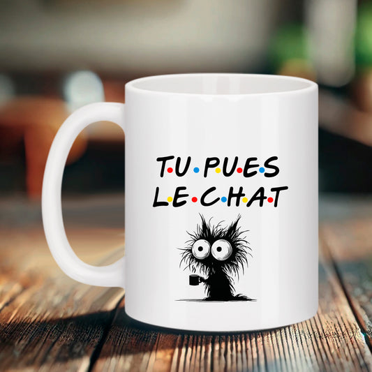 Mug blanc Bruhle avec le texte "TU PUES LE CHAT" écrit dans la police de la série Friends, illustré d'un petit chat noir ébouriffé tenant une tasse de café.